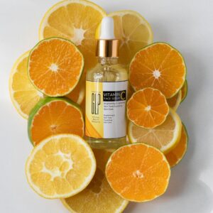 Vitamin C serum bottle surrounded by fresh orange and lemon slices.